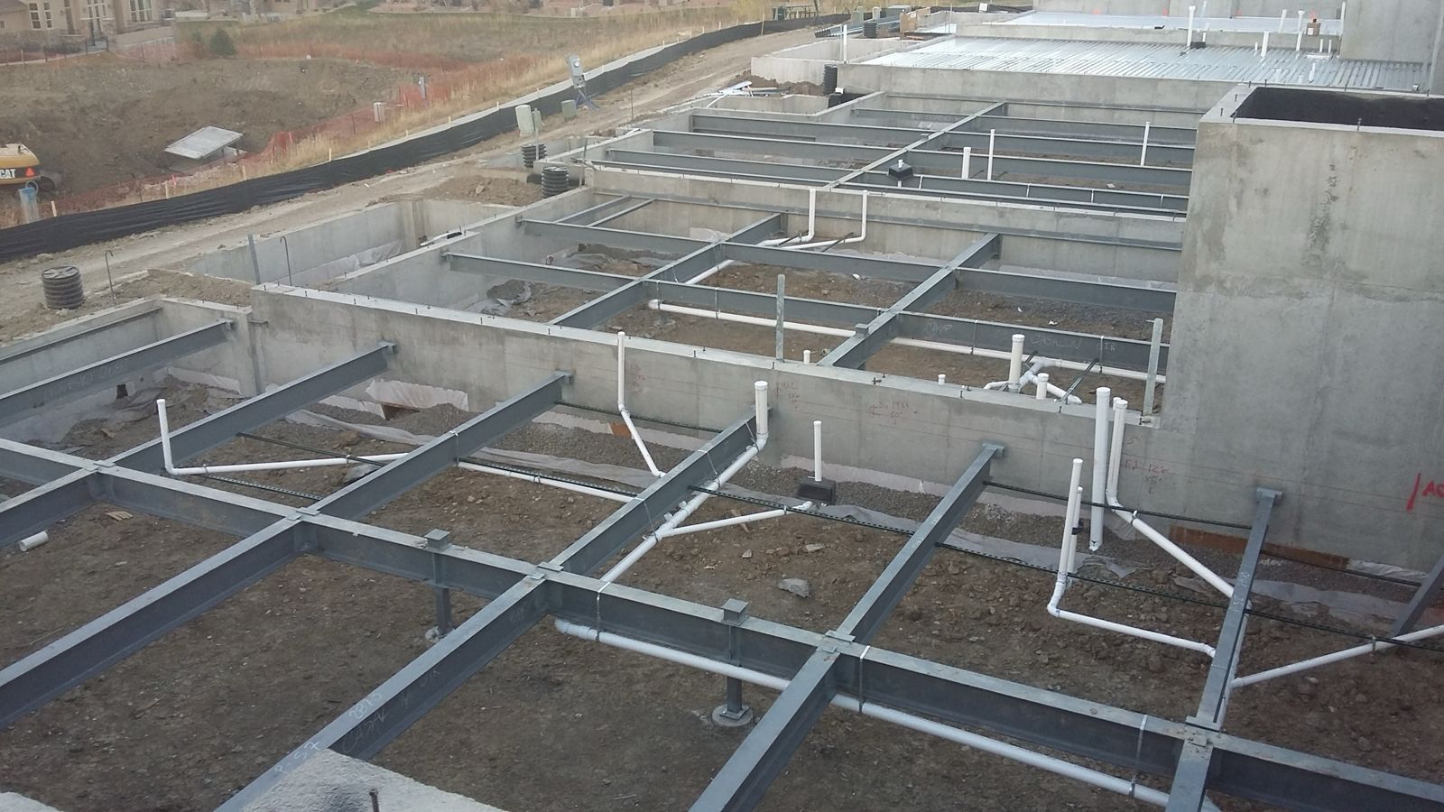 Steel structural floor beams set over basement plumbing, ready for decking
